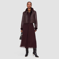 Model wearing the JOSEPH Ale silk chiffon trousers in mahogany with a shearling jacket and black boots