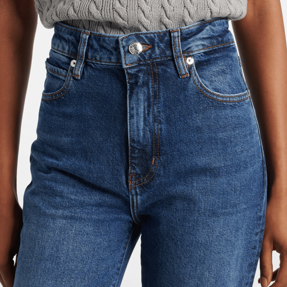 Close-up of FRAME The Arrow jeans in Rival at Riada Concept. High-rise blue bootcut jeans in comfort-stretch denim with a 33-inch inseam - showing waistband and front pockets
