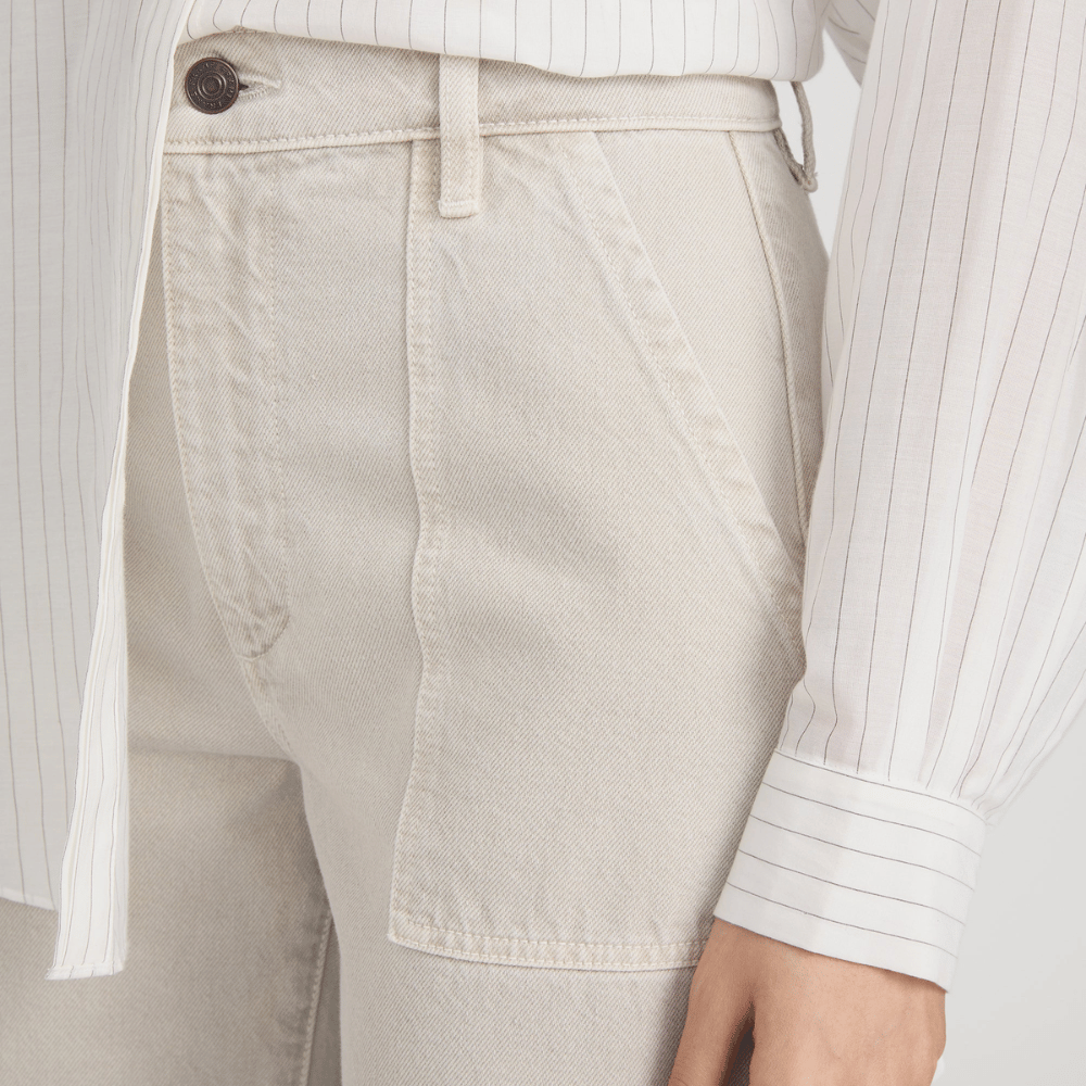 Close-up of model wearing the FRAME The Bow Cargo Jeans in Flax at Riada Concept. High-rise rigid denim with flat utility pockets and a sculpted barrel leg - white pinstriped shirt tucked in, showing the waistband, button, belt loop, and front pocket area.