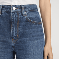 Close-up of a person wearing FRAME The Bow Jeans in Acumen New Fray at Riada Concept. High-rise rigid denim with a sculpted barrel leg and raw frayed hem -  with visible waistband, belt loops, front pocket, and stitching