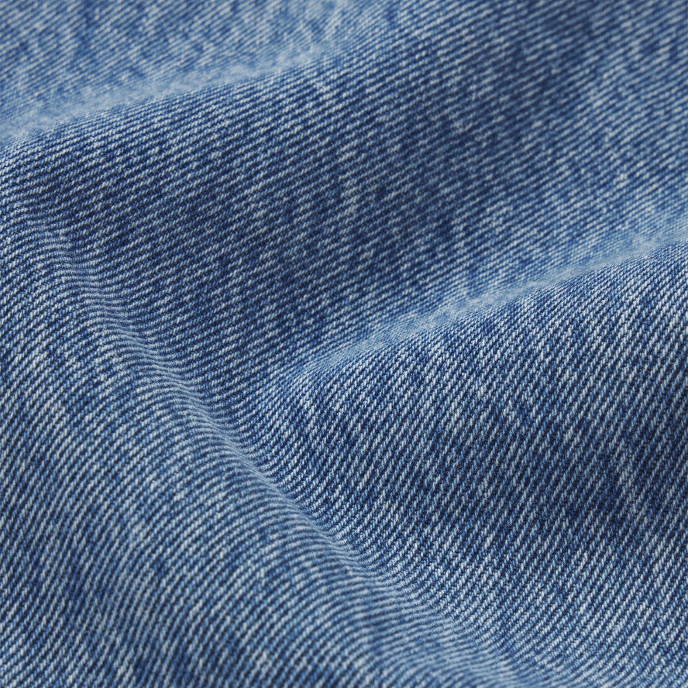 A close-up the FRAME The Essential Jean in Rapture at Riada Concept. Mid-rise full-length straight jeans in rigid regenerative cotton denim -  blue denim fabric with visible twill texture and soft folds