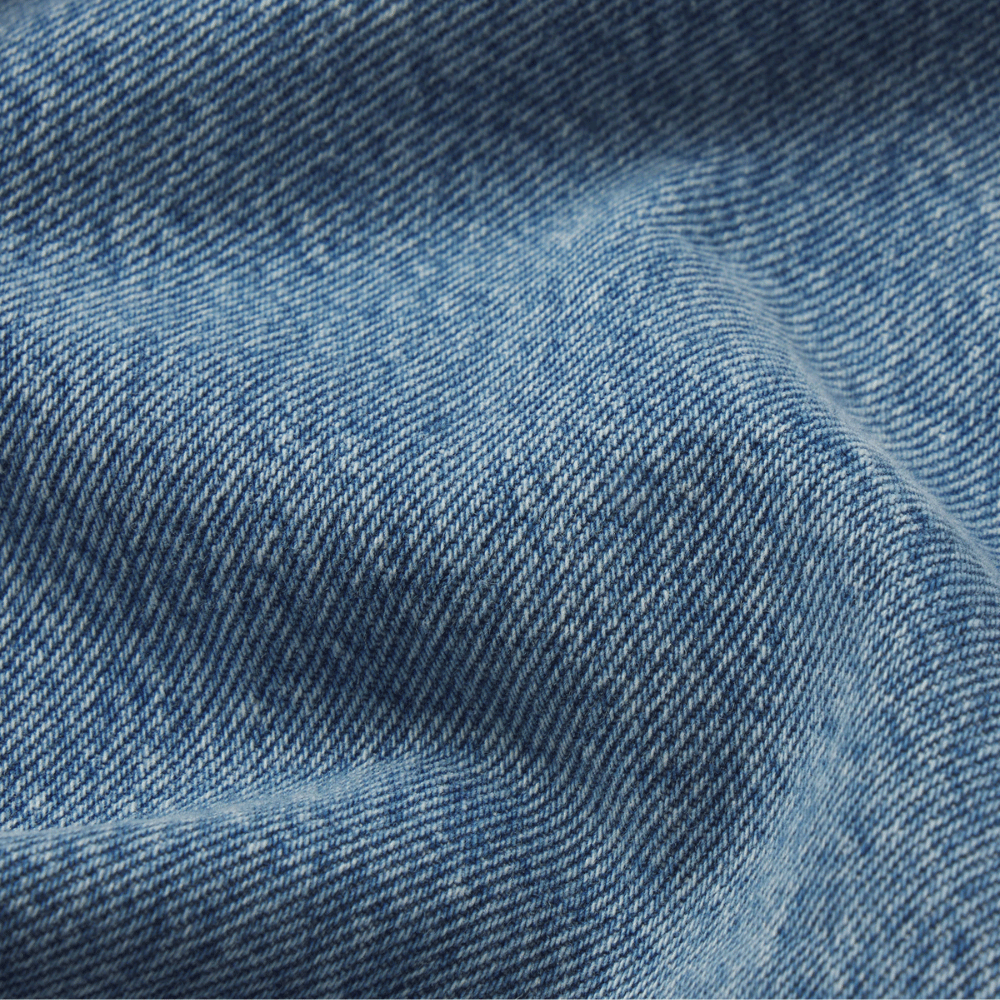 Close-up of blue denim fabric with a visible twill weave and soft folds - FRAME The Gray Jean in Rapture at Riada Concept. Low-rise rigid denim with a long wide-leg flare, button fly and 34-inch inseam - front view