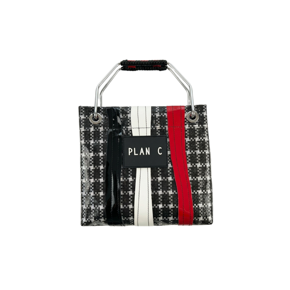 A small structured handbag with a black and white plaid pattern, featuring vertical stripes in black, white, and red, and a central black label with the text 'PLAN C'. It has a silver metal top handle with a black grip.