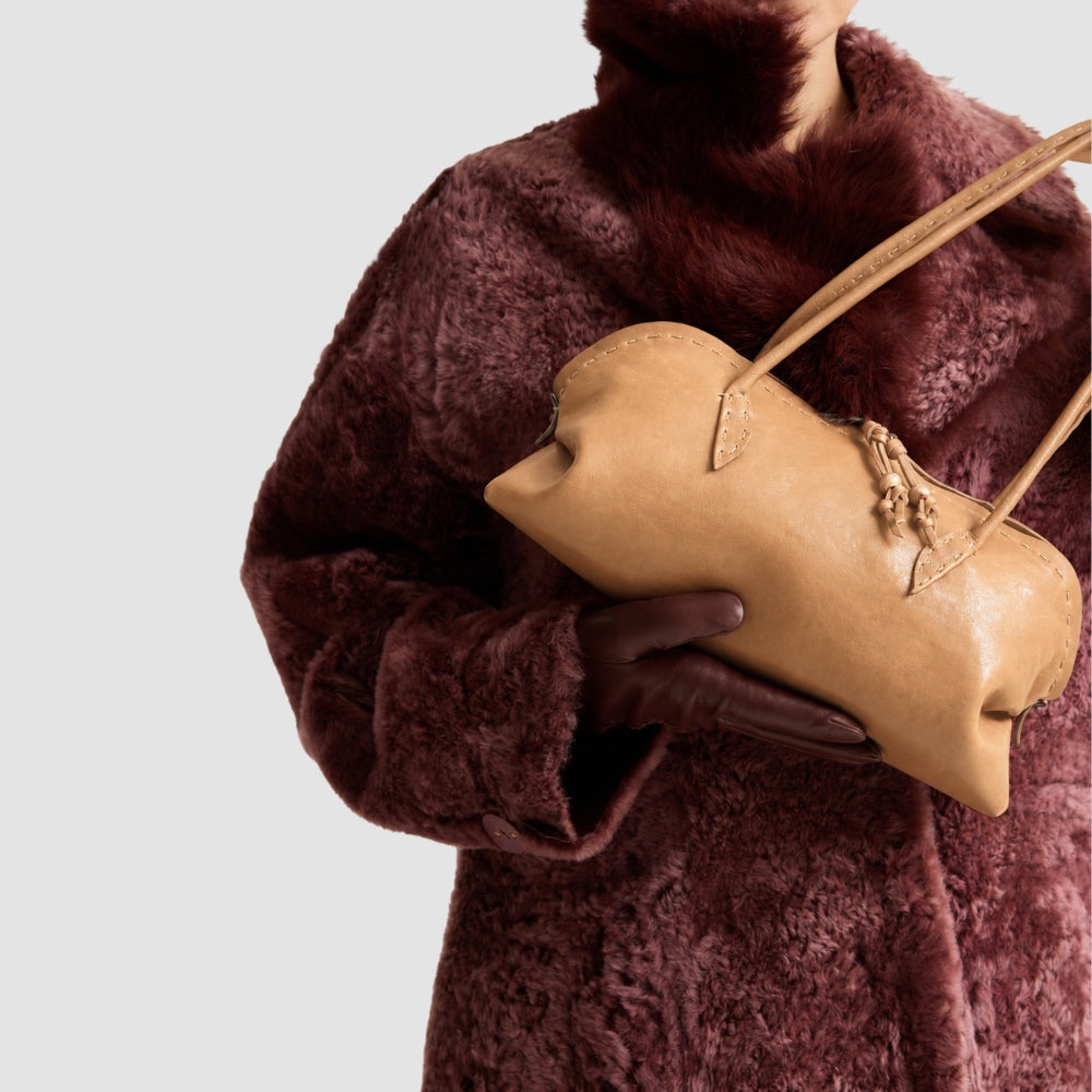 Riada Concept Henry Beguelin’s Bolla Bassa in camel Old Iron lambskin: a low, elongated shoulder bag, hand-worked in Italy, that softens and deepens in colour with wear - styled model