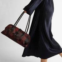 Riada Concept Henry Beguelin’s Bolla Bassa in streaked wine pony-hair calf: a low, rounded shoulder bag with black leather handles and beaded pulls, handcrafted in Italy - styled model