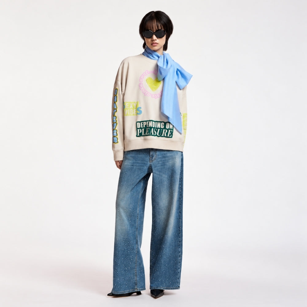 Riada Concept Essentiel Antwerp relaxed cream cotton sweatshirt, covered in colourful slogans, with a sequinned heart, beaded sleeve lettering and a 1999 back panel, full model front view