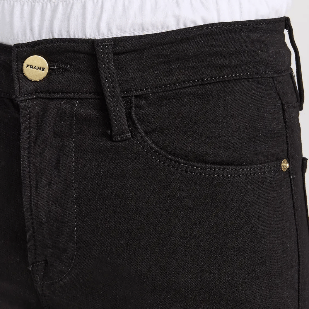 Close-up of FRAME Le High Straight Ankle Jeans in Film Noir at Riada Concept. High-rise slim straight jeans in ultra-stretch black denim - showing the front waistband, belt loops, button closure with a gold-tone 'FRAME' button, and the front pocket.
