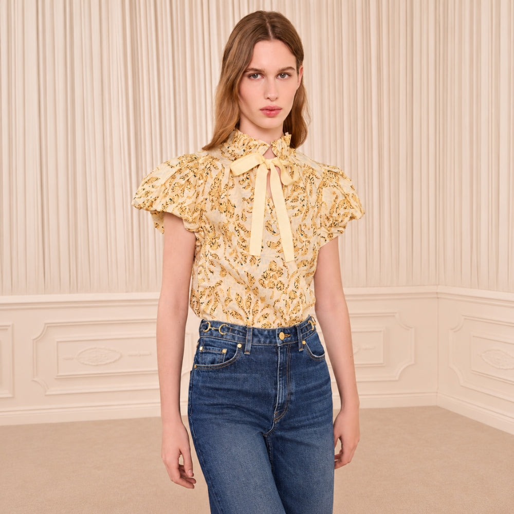 Riada Concept Ulla Johnson Estela cotton poplin top in a pale yellow print, with bubble sleeves and a ruffled tie neck - styled model front view 